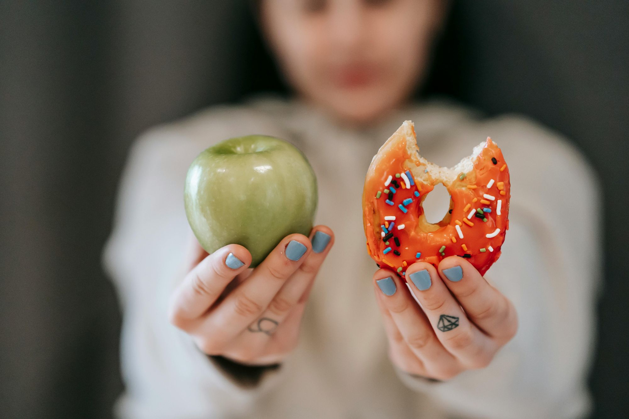 Picture of woman holding apple in one hand and doughnut in other hand